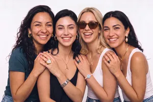 Four women smiling together in white studio